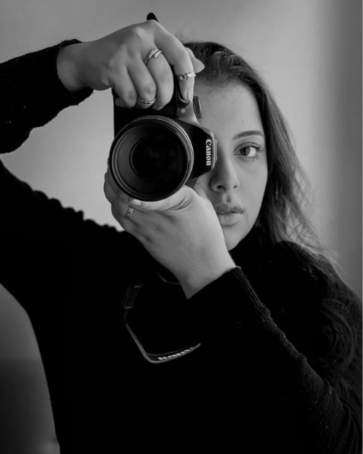 Clarissa Lopes, em preto e branco, segurando uma câmera Canon próxima ao rosto